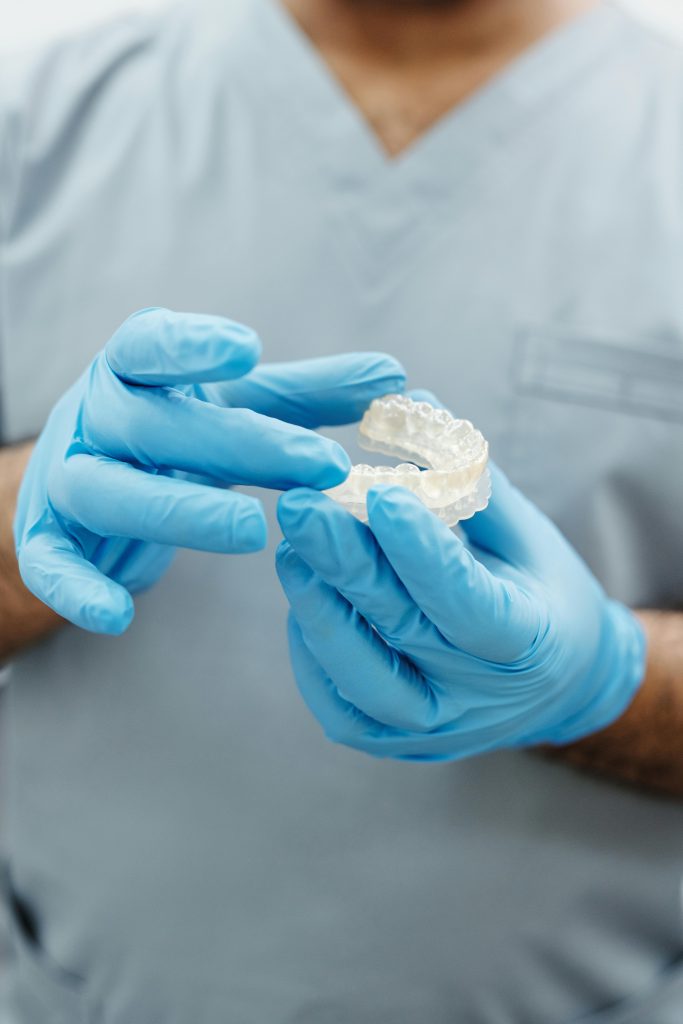 pexels-photo-4270079-4270079 Dentist wearing blue gloves examining a dental mold in a clinical setting.